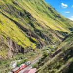 train on railway between green mountains during daytime
